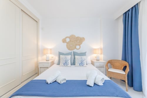 Modern bedroom at Marbella Home Rentals with blue accents, dual lamps, wicker chair, and coastal decor