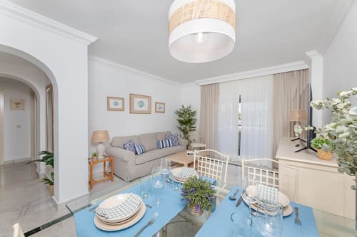 Bright open-plan dining and living area in Marbella apartment with blue table, beige sofa, and modern furnishings
