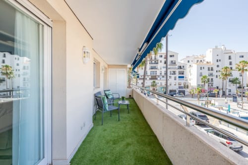 Modern apartment balcony in Marbella with artificial turf, lounge chairs, and city views of Puerto Banus