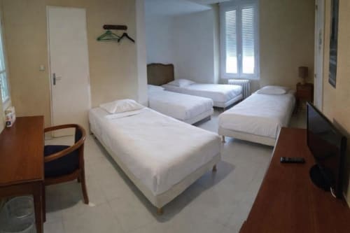 Quad room at Hotel de Champagne in Saint-Dizier with three single beds, wooden furniture, and bright windows