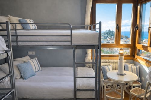 Literas modernas con vista al mar, ciudad costera y horizonte atlántico visibles a través de puertas de madera en el apartamento Holibai de Baiona