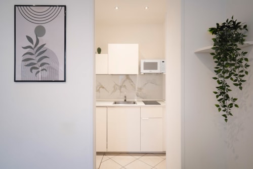 Modern kitchenette at IV House Rome with cream cabinetry, marble backsplash, microwave, and minimalist botanical decor