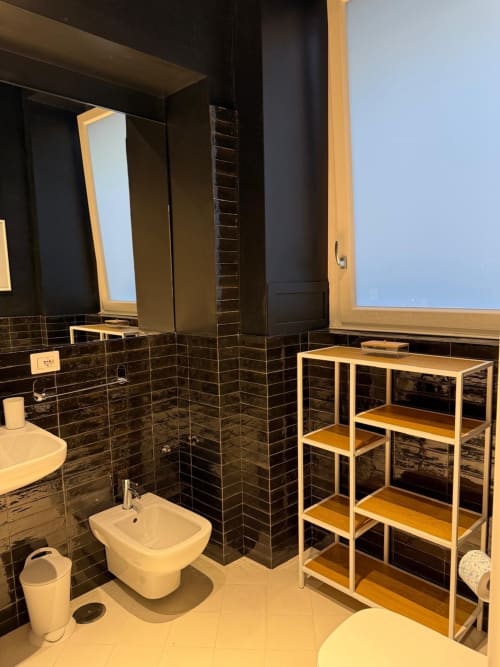 Bagno moderno a Tresette Porta Capuana, Napoli, con doccia in piastrelle nere, bidet bianco, ripiani in legno e ampio specchio