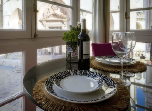 Mesa de comedor elegante en la Suite Catedral, Burgos con vistas a la ciudad a través de grandes ventanales, botella de vino y servicio de mesa.