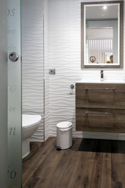 Baño moderno en la Suite Catedral del hotel Burgos con paredes de azulejos texturados blancos, tocador de madera oscura y espejo enmarcado