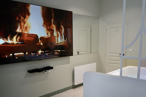 Salle de bains moderne avec écran plat diffusant un foyer, mobilier blanc et douche vitrée à La Maison D'olivier