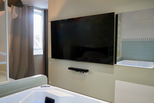 Salle de bain moderne avec écran plat mural, baignoire chaude et douche au gîte La Maison D'olivier en France