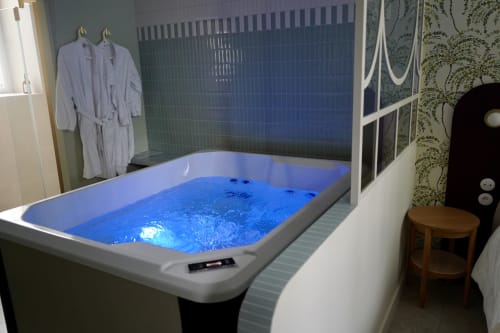 Baignoire moderne avec eau illuminée en bleu dans la salle de bains du gîte La Maison D'olivier, avec peignoirs et équipements