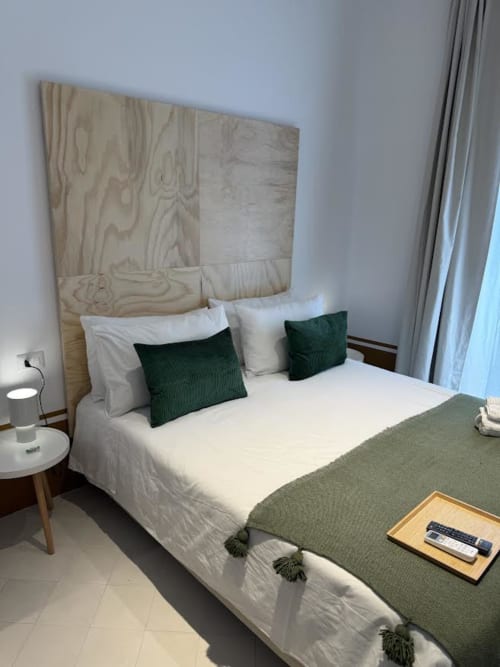 Camera moderna dell'hotel Tresette Porta Capuana a Napoli con testata in legno, biancheria bianca, cuscini verdi e vista sulla città