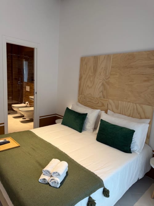 Camera dell'hotel Tresette Porta Capuana a Napoli con testata in legno, biancheria bianca, cuscini verdi e bagno in camera