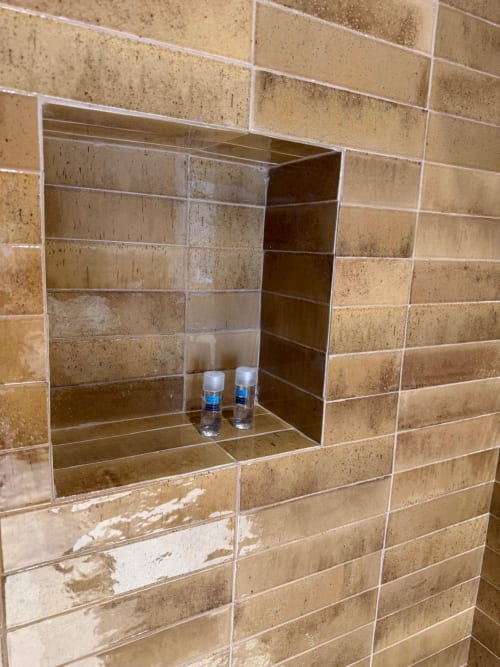 Nicchia da bagno con rivestimento in travertino nella suite dell'hotel Tresette Porta Capuana a Napoli, con due flaconi di cosmetici e bianco