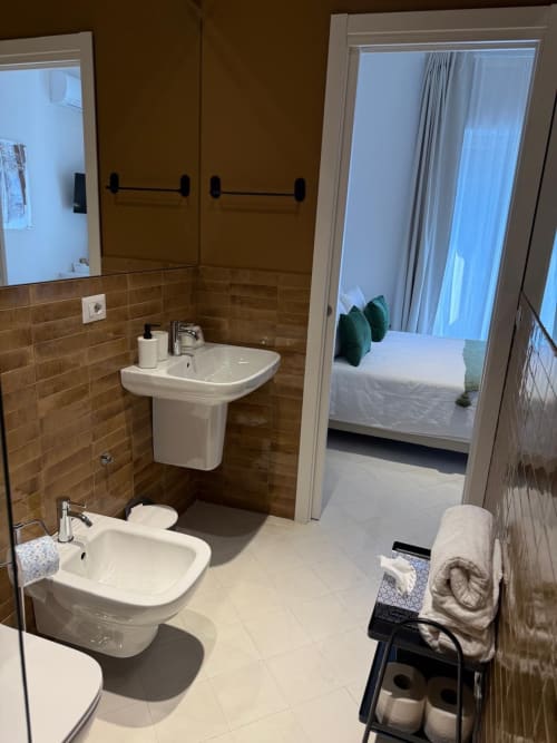 Moderno bagno di Tresette Porta Capuana a Napoli con doppio lavabo, pareti piastrellate marrone e vista sulla camera con cuscini verdi