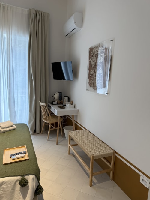 Camera moderna dell'Hotel Tresette Porta Capuana a Napoli con scrivania, TV, poltrona verde, panca in legno e aria condizionata