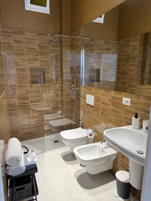 Bagno moderno all'hotel Tresette Porta Capuana di Napoli con doccia in vetro, bidet, doppio lavabo e piastrelle beige