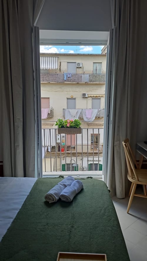 Camera da letto con letto verde e asciugamani arrotolati affacciata sui balconi di Napoli presso l'hotel Tresette Porta Capuana