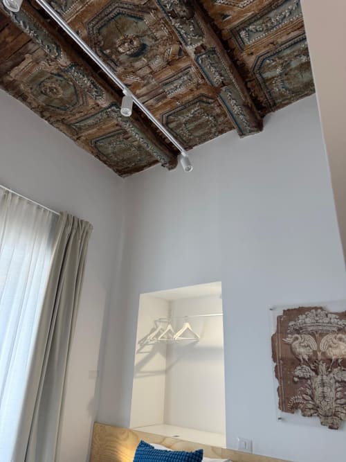 Soffitto in legno ornato e storico con intarsi metallici decorativi nella camera d'hotel di Napoli, pareti bianche e servizi moderni sottostanti