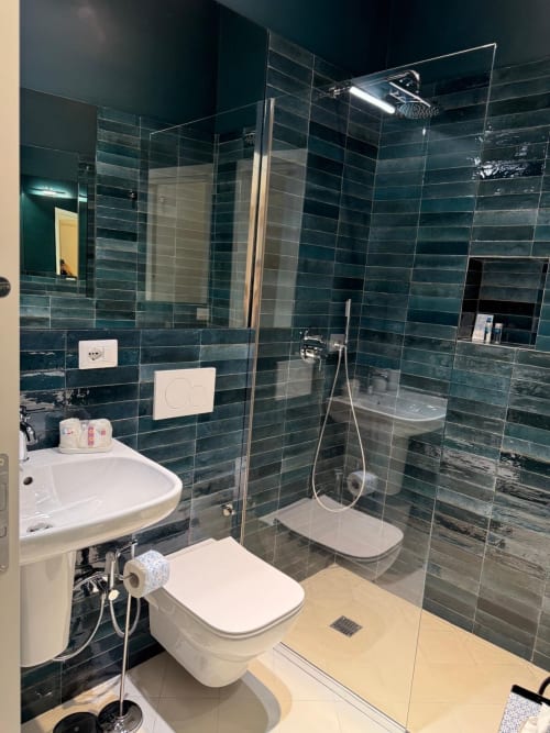 Bagno moderno dell'hotel Tresette Porta Capuana a Napoli con piastrelle blu turchese, doccia in vetro, lavabo bianco e