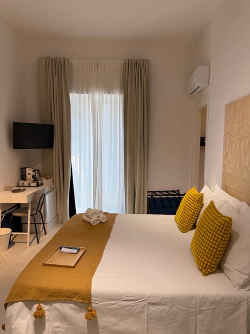 Camera d'albergo moderna al Tresette Porta Capuana di Napoli con letto bianco, cuscini gialli, scrivania, TV e balcone con vista su landmark