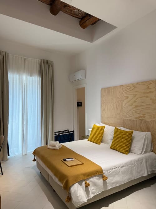 Camera moderna dell'hotel Tresette Porta Capuana a Napoli con testata in legno, biancheria bianca e cuscini gialli accento