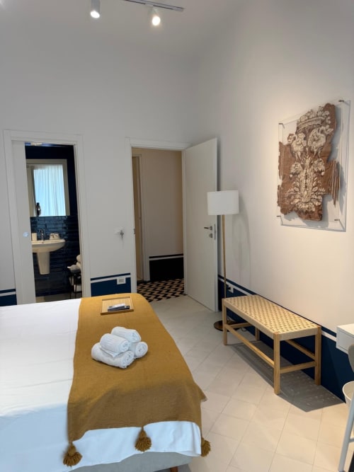 Ampia camera moderna all'Hotel Tresette Porta Capuana di Napoli con letto, bagno, panchetta in legno, opere d'arte e vista sulla città