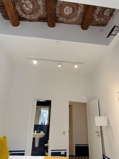 Camera moderna al Tresette Porta Capuana di Napoli con travi in legno a vista, pareti bianche, illuminazione a binario e porte d'accesso a