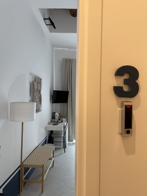 Ingresso della camera 3 dell'hotel Tresette Porta Capuana a Napoli, con corridoio, lampada da tavolo e segnaletica del numero della stanza