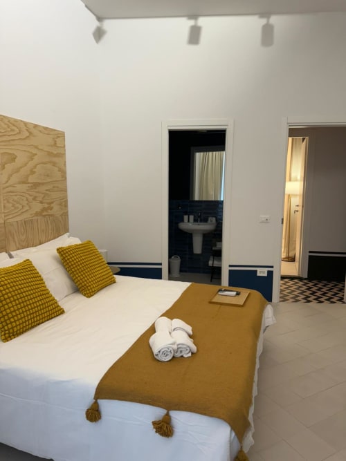Camera moderna dell'hotel Tresette Porta Capuana a Napoli con cuscini gialli, letto bianco e bagno privato con lavabo su colonna