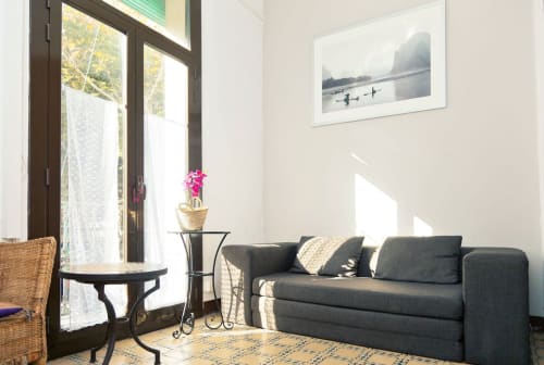 Sala de estar de apartamento moderno en Barcelona con sofá gris, luz natural del balcón y cuadro con vista de la ciudad