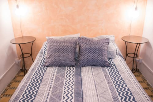 Dormitorio moderno en apartamento de Barcelona con ropa de cama azul estampada, almohadas decorativas y mesillas gemelas con lámparas