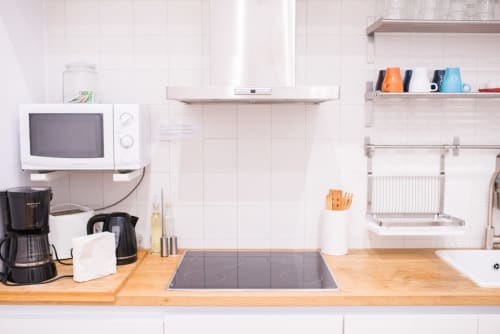 Cocina moderna en apartamento de Barcelona con encimera de madera, placa de cocción eléctrica, microondas, cafetera y estantería mural