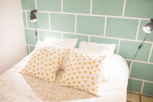 Dormitorio moderno con pared de azulejos verde menta, ropa de cama blanca y almohadas amarillas con lunares en apartamento de Barcelona
