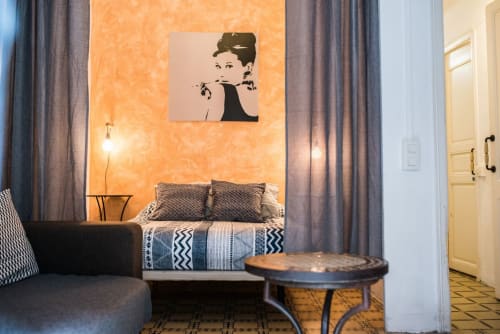 Dormitorio de apartamento en Barcelona con pared de acento naranja, cama, obra de arte retrato en negro y mobiliario moderno