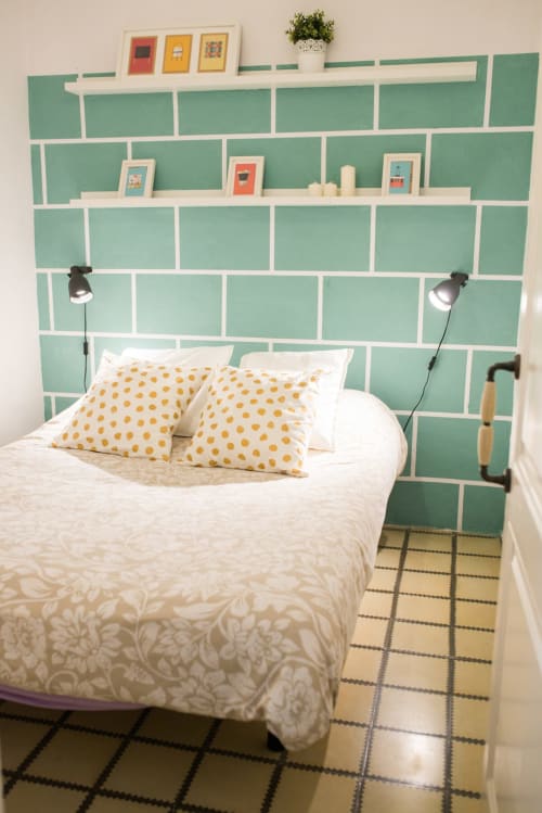 Acogedora habitación de apartamento barcelonés con cabecero de azulejos verde menta, almohadas amarillas con lunares y lámparas de lectura junto a la cama