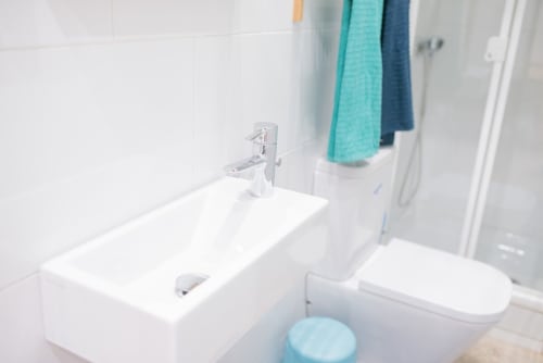 Baño moderno en apartamento de Barcelona con lavabo blanco, grifo cromado, inodoro y cabina de ducha. Toallas colgadas en