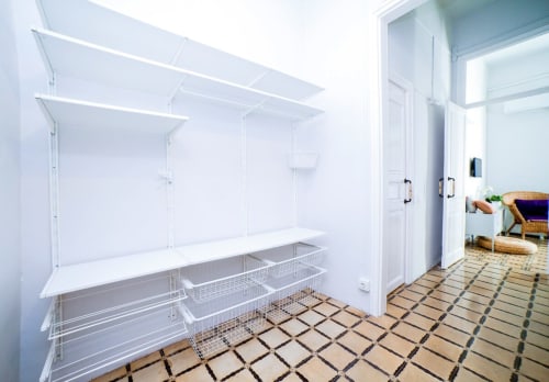 Vestidor vacío con estanterías blancas y cestas de almacenamiento de rejilla en apartamento de Barcelona