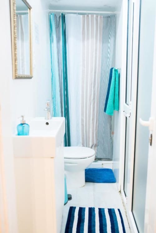 Baño moderno en apartamento de Barcelona con lavamanos blanco, inodoro, cortina de ducha a rayas, toallas azules y accesorios