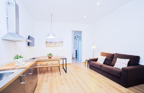 Sala de estar moderna en apartamento de Barcelona con cocina integrada, comedor, sofá marrón y suelos de madera