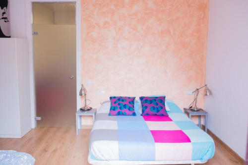 Dormitorio luminoso en apartamento barcelonés con ropa de cama colorida, lámparas gemelas, paredes texturizadas melocotón y suelo de madera