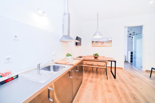 Cocina y comedor de apartamento moderno en Barcelona con mesa de madera, fregadero de acero inoxidable e iluminación colgante