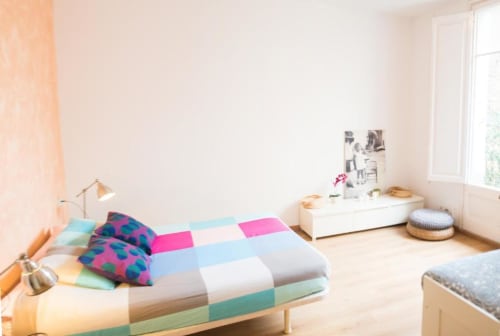 Luminoso dormitorio de apartamento en Barcelona con ropa de cama colorida, luz natural, muebles modernos y vista a la ciudad