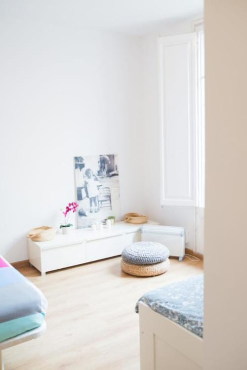 Sala de estar de apartamento moderno en Barcelona con almacenamiento blanco, pufos tejidos, luz natural y muebles contemporáneos