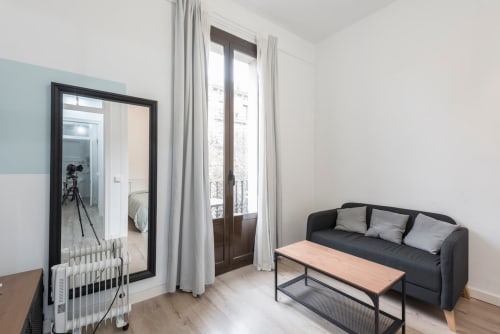 Sala de estar de apartamento moderno en Barcelona con sofá negro, mesa de madera y puertas francesas con vistas a la ciudad