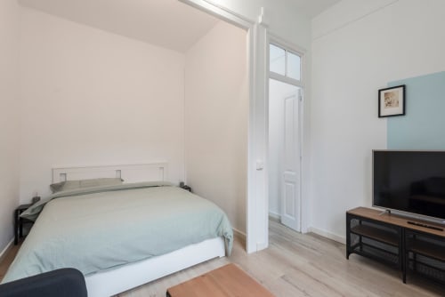 Dormitorio de apartamento reformado moderno en Barcelona con cama, TV y decoración minimalista