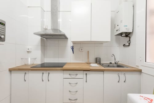Cocina moderna blanca con encimera de madera, electrodomésticos de acero inoxidable y cocina de gas en apartamento de Barcelona