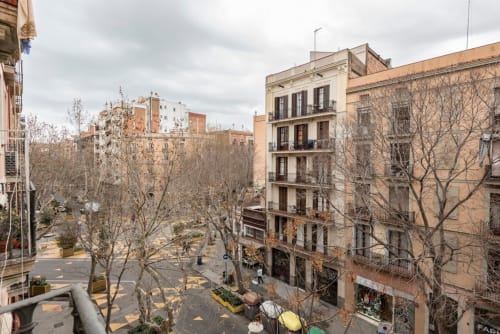 Plaza de Barcelona con edificios residenciales, árboles desnudos y peatones - vista desde apartamento renovado con balcón