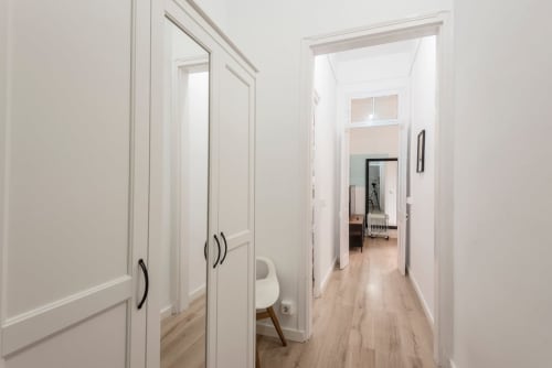 Pasillo luminoso en apartamento barcelonés con puertas blancas, suelos de madera y acabados modernos que conducen a varias habitaciones