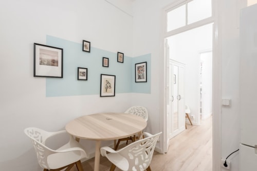 Zona de comedor moderna en apartamento de Barcelona con mesa redonda, sillas blancas, suelos de madera clara y cuadros en la pared