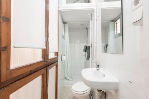Baño moderno en apartamento de Barcelona con lavabo blanco, inodoro, cabina de ducha y espejo