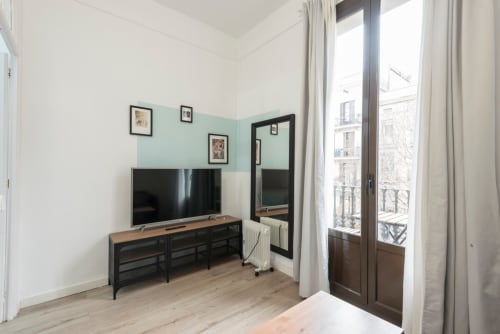 Sala de estar moderna en Barcelona con TV, consola multimedia negra, pared acento en menta y puertas al balcón con vistas a la ciudad