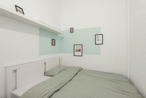 Habitación minimalista en apartamento de Barcelona con pared accent en verde menta, cama blanca y cuadros sobre cabecera